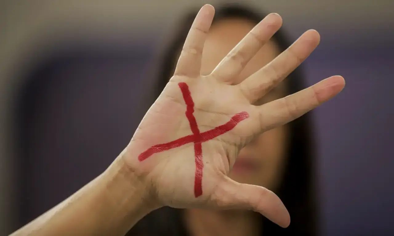 Mulher cobrindo o rosto com a mão, onde está marcado um "X"vermelho