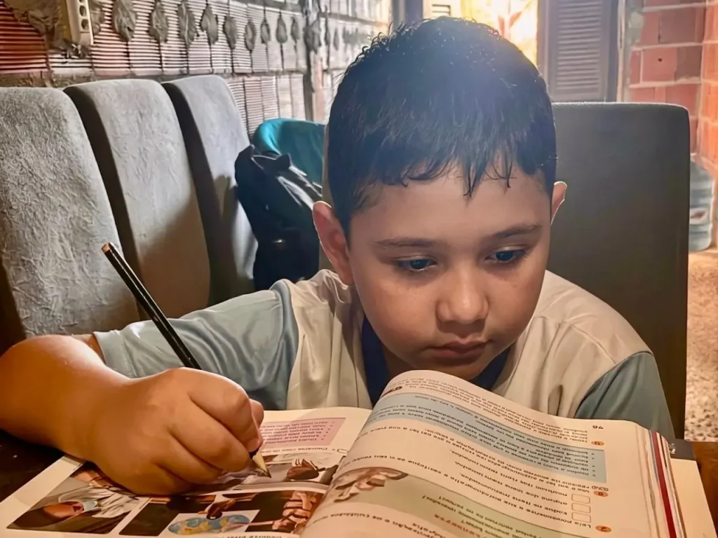 Davi Santos, de 9 anos, estudando com um livro sobre mesa na sala de casa