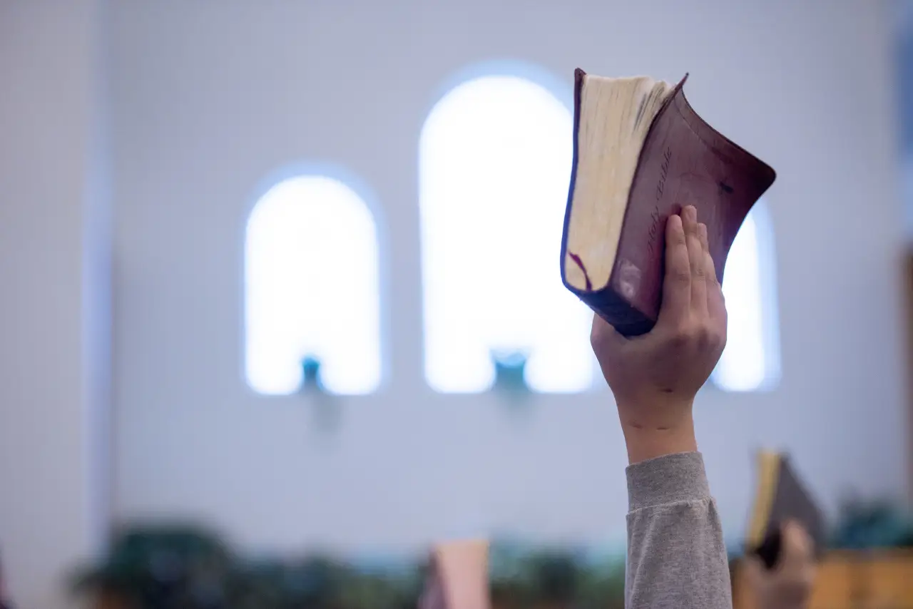 Homem levanta a mão segurando uma Bíblia em igreja